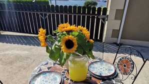 Un tavolo esterno rotondo con piastrelle decorate a mosaico, un vaso con girasoli e un bicchiere di succo di frutta.