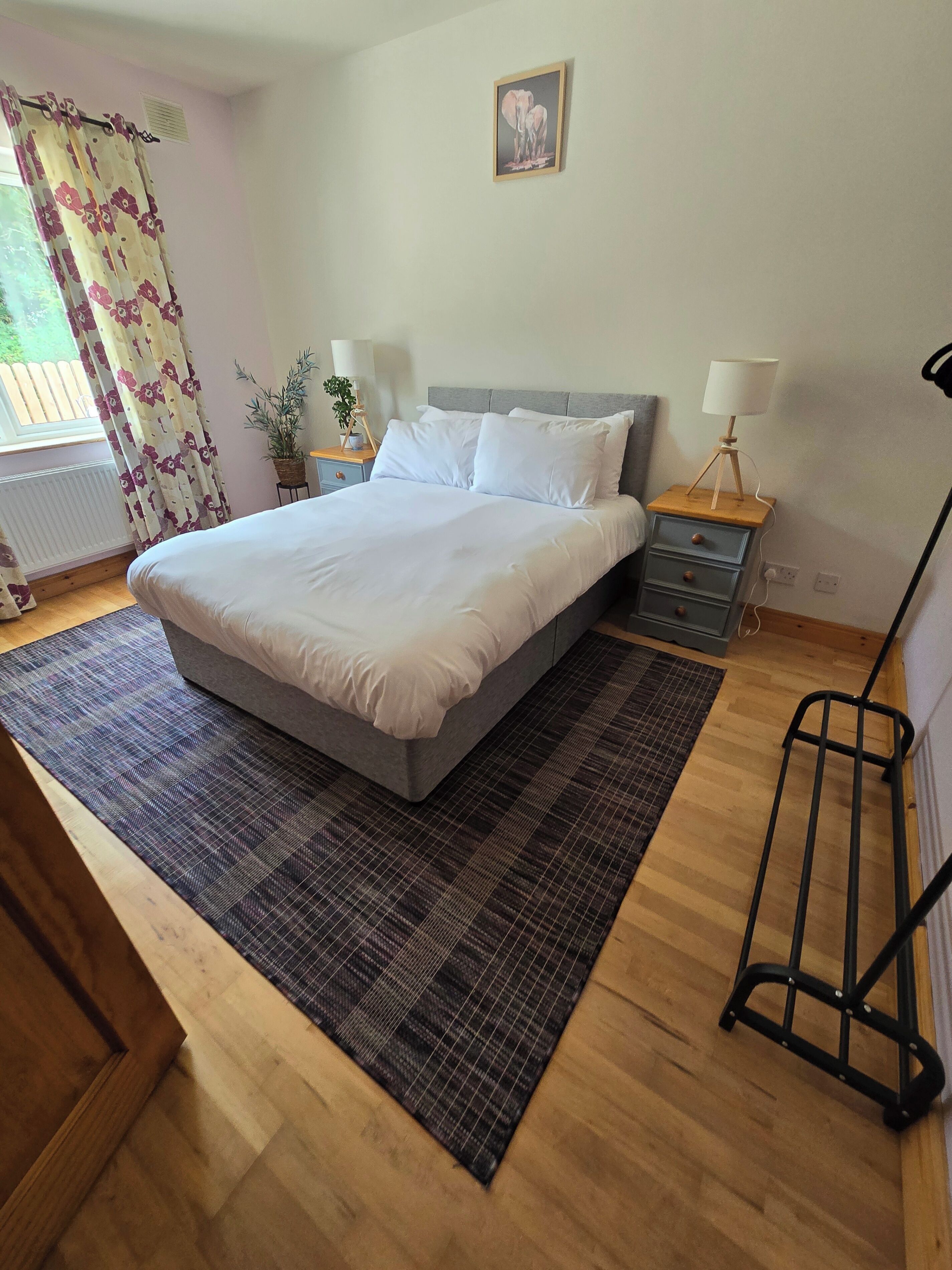A bedroom with a large bed, a bedside table with a lamp, a small plant, and a radiator.