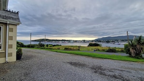 Vista sulla costa con un vialetto sterrato che conduce a una casa con tetto spiovente.