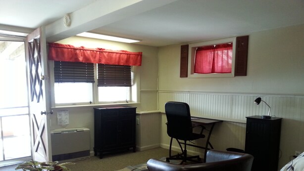 A room with a desk, chair, radiator, window with blinds, and a potted plant.