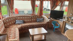 A cozy living area with a sofa, a small table, a TV, and a window with curtains. - 2-bed -Sleeps 4 - Parking - Pets - 5 mins to Beach (Chapel St Leonards)
