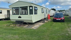 A mobile home with a front porch and a car parked nearby. - 2-bed -Sleeps 4 - Parking - Pets - 5 mins to Beach (Chapel St Leonards)