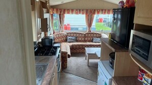A compact RV interior with a kitchenette, a sofa, and a television. - 2-bed -Sleeps 4 - Parking - Pets - 5 mins to Beach (Chapel St Leonards)