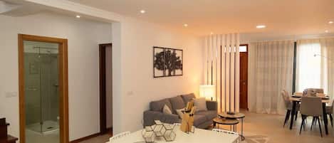 A modern living room with a sofa, dining table, and a glass shower enclosure.