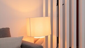 Ein Zimmer mit grauem Sofa, einer Lampe und vertikalen Rollläden.