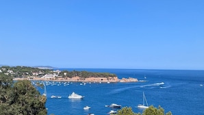 Un pueblo costero con un puerto deportivo lleno de barcos, un cielo azul despejado y vistas al mar.