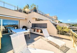 A modern outdoor dining area with a glass enclosure, a barbecue grill, and a kitchen area with a sink and countertop.