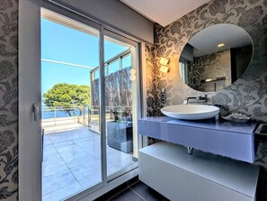 A modern bathroom with a large sliding glass door leading to a balcony, a round mirror, and a white sink.