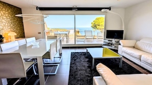 Una sala de estar moderna con comedor, un sofá, un televisor y vistas al mar a través de grandes puertas correderas.