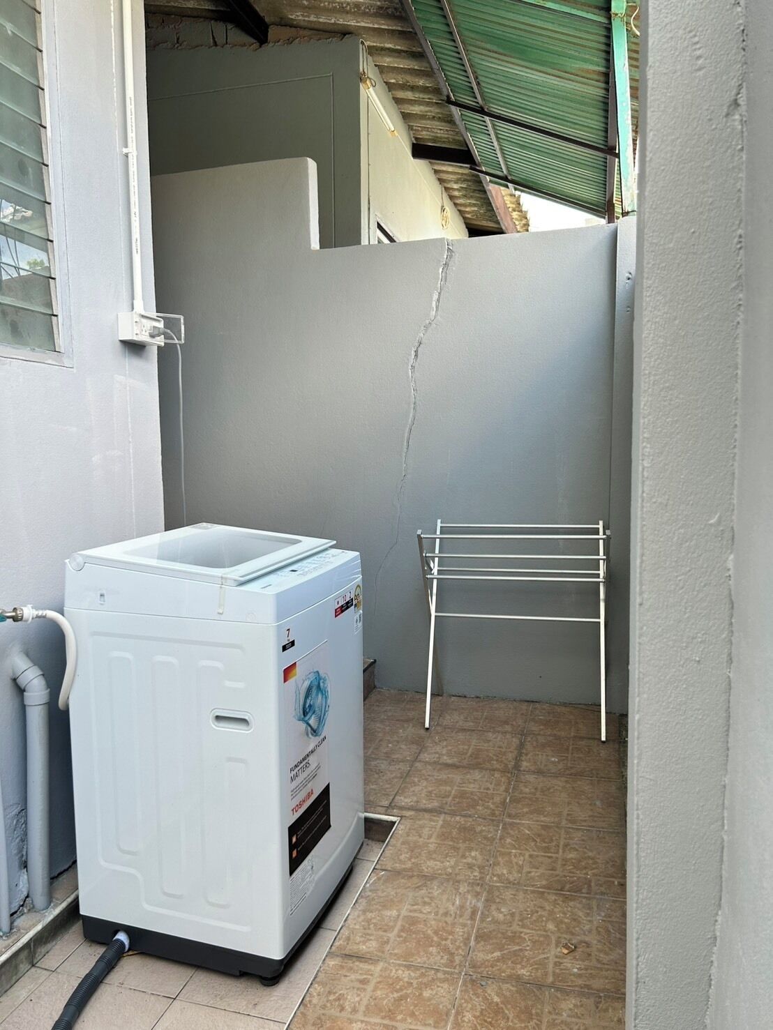 Un área de lavandería compacta con lavadora, tendedero y piso de baldosas.