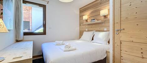 A bedroom with a bed, a desk, a window, and a door.