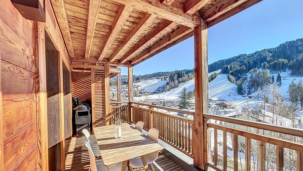 Una terraza de madera con mesa y sillas, con vistas a un paisaje nevado.