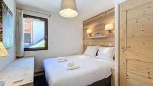 Un dormitorio con cama, una mesita de noche, una ventana con cortinas, un armario de madera y una lámpara colgante.
