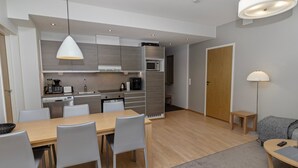 A modern kitchen with grey cabinets, a dining area with a wooden table and chairs, and a small seating area with a sofa and a lamp. - Ruka chalets 2 huoneisto 2405 by Interhome (Kuusamo)