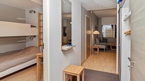 A compact hotel room with a bunk bed, a small wooden table, a mirror, and a sofa in the adjacent living area. - Ruka chalets 2 huoneisto 2405 by Interhome (Kuusamo)