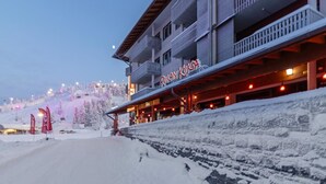 A hotel with a sign reading "Pukan Kuksa" on the facade, surrounded by snow-covered terrain and a ski lift in the background. - Ruka chalets 2 huoneisto 2405 by Interhome (Kuusamo)