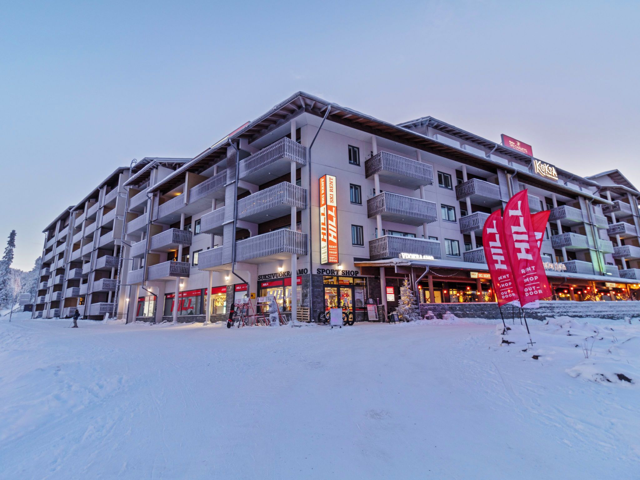 Ein mehrstöckiges Hotel mit Balkonen, Skiverleihschildern und einem Sportgeschäft.