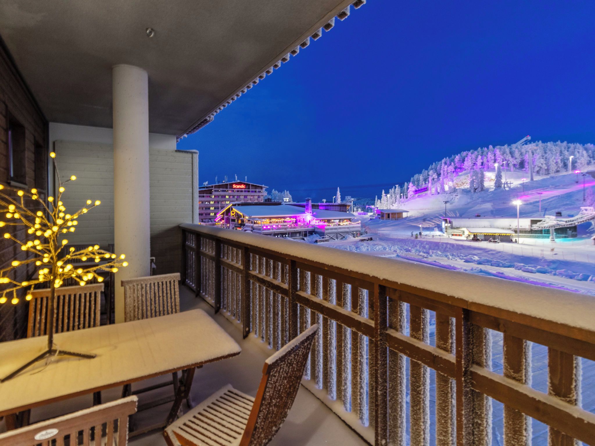 Un balcon donnant sur un paysage enneigé, avec un bâtiment illuminé en arrière-plan.
