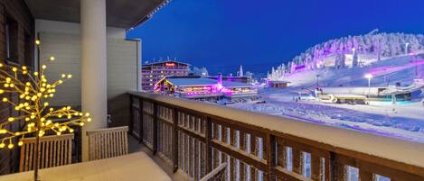 A balcony with a view of a snow-covered landscape and a lit-up building in the background.
