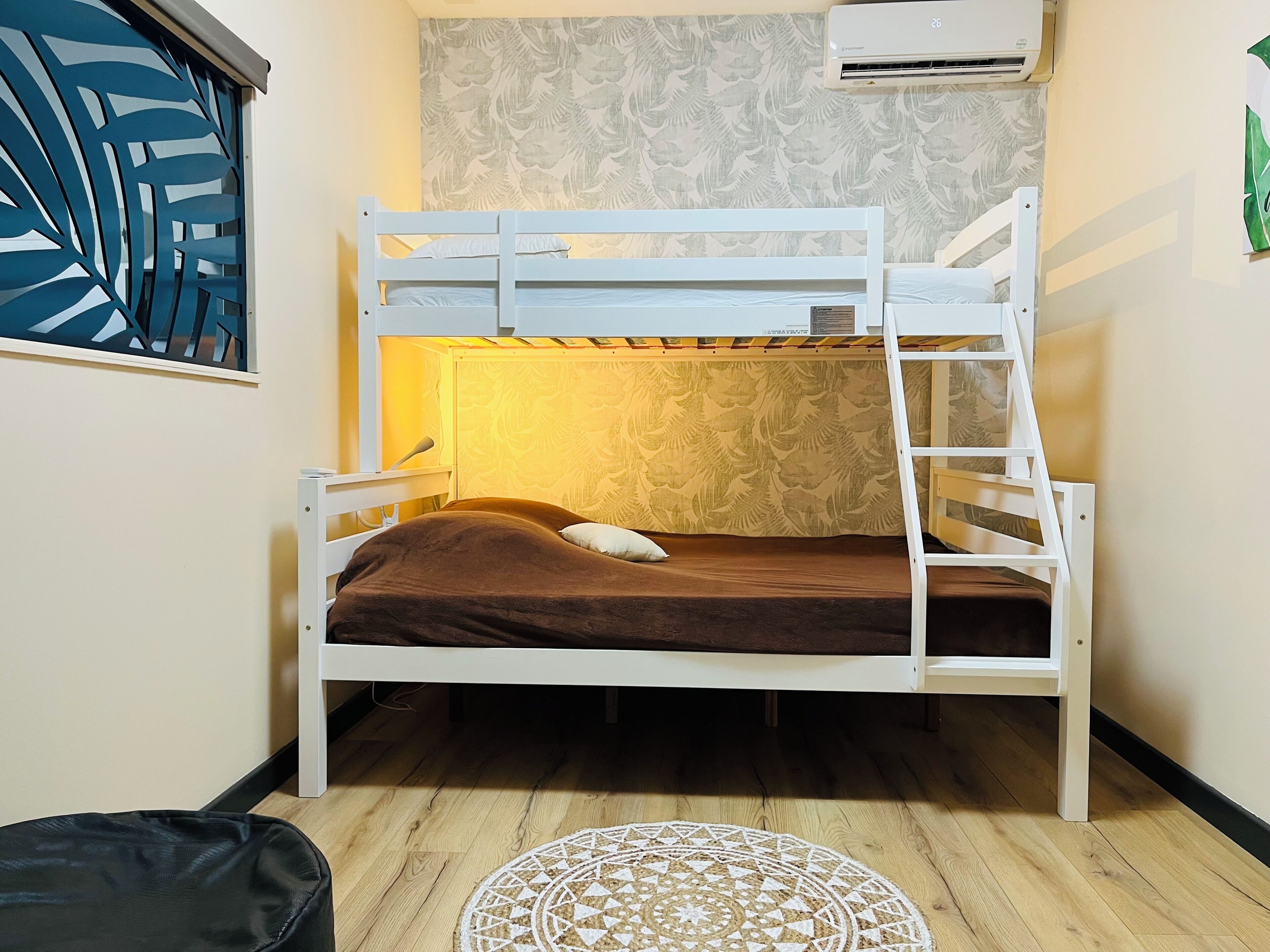 A bunk bed with a brown mattress and pillows, a white headboard, and a patterned wall behind it.
