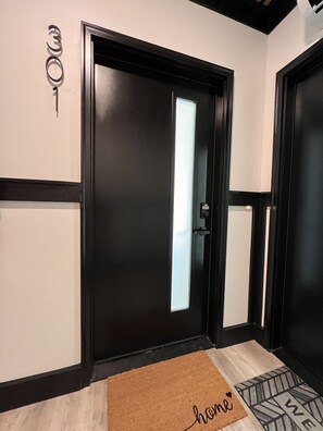 A black door with a glass panel, a doormat with 'home' written on it, and a wall-mounted sign with the number '301'.