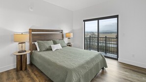 A bedroom with a large bed, two bedside tables with lamps, a wooden headboard, and a balcony with a view. - Juneau Family Friendly Getaway 301 (Juneau)