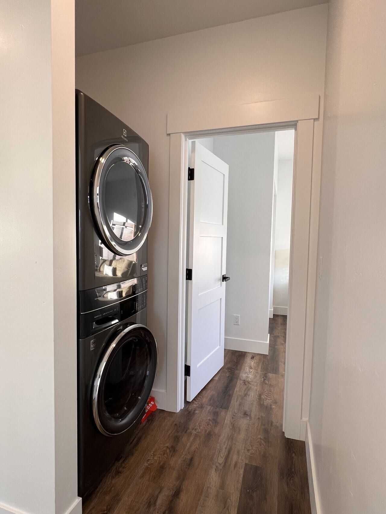 Une buanderie avec des machines à laver et des sèche-linge superposés, une porte blanche et un plancher en bois.