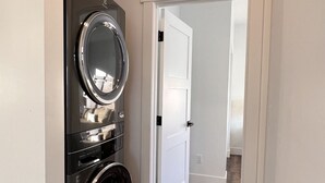 A laundry room with stacked washers and dryers, a white door, and a wooden floor. - Juneau Family Friendly Getaway 301 (Juneau)