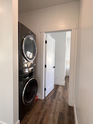 A laundry room with stacked washers and dryers, a white door, and a wooden floor.