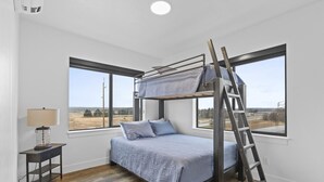 A bunk bed room with a ladder, a lamp, and large windows with a view. - Juneau Family Friendly Getaway 301 (Juneau)