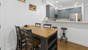 A dining area with a wooden table and chairs, a kitchen with grey cabinets, and pendant lighting. - Accessible, Comfort, Convenient Location 106 (Juneau)
