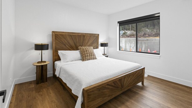 A bedroom with a wooden bed, white bedding, two bedside tables with lamps, and a window with a view of trees and a fence. - Accessible, Comfort, Convenient Location 106 (Juneau)