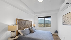Un dormitorio con cama, dos lámparas de noche, una ventana con vistas y una obra de arte en la pared.
