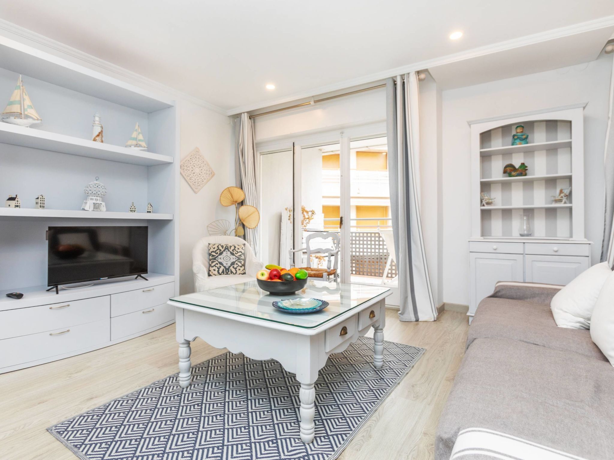 A modern living room with a TV, a glass-top coffee table with fruits, a sofa, and a bookshelf.