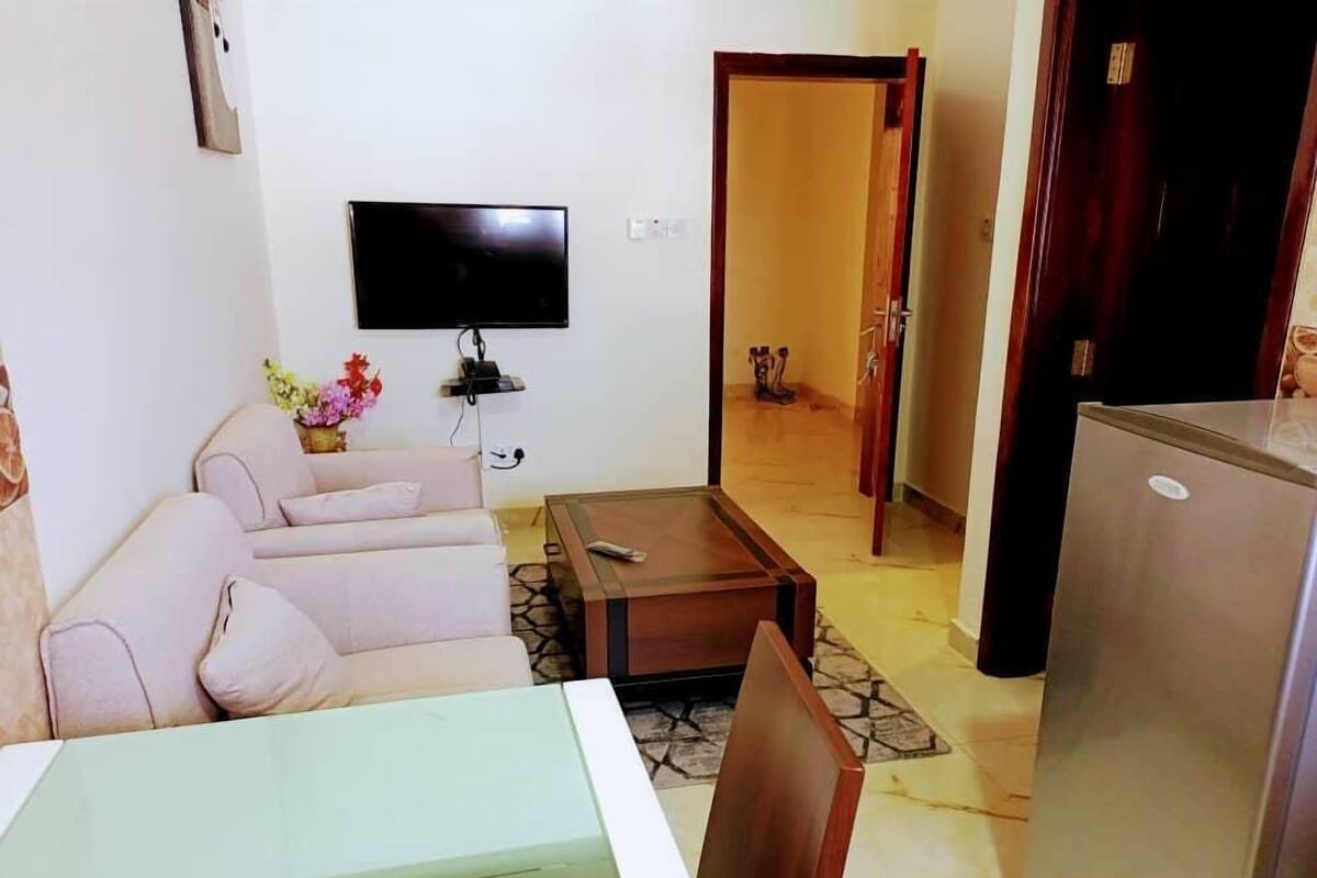 A living room with a sofa, a coffee table, a TV, and a refrigerator.