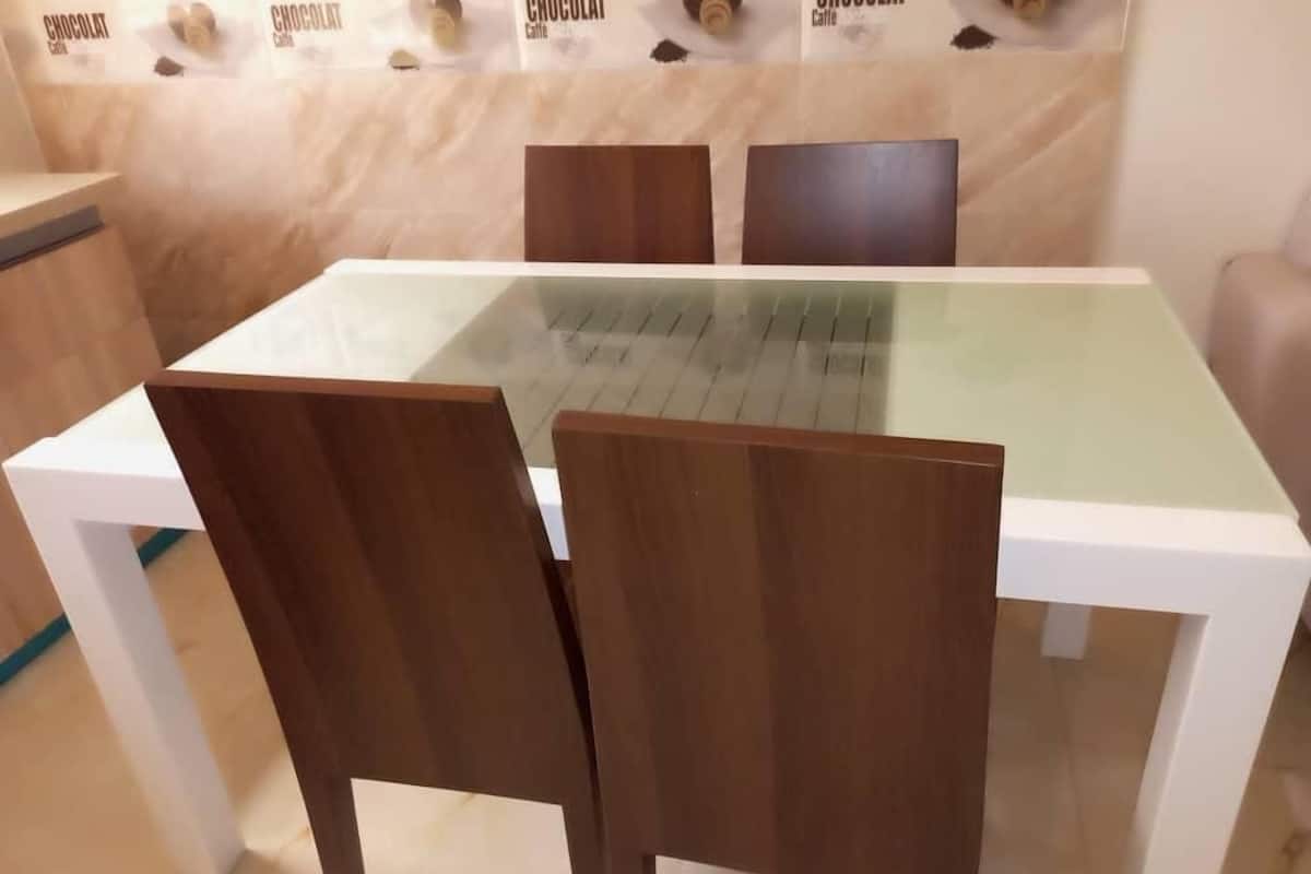 A dining table with a glass top and wooden chairs.