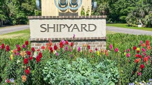 Un letrero con la palabra 'SHIPYARD' y un logotipo, rodeado de flores coloridas.