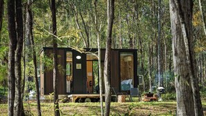 A small cabin in a forest with a deck and a large window.