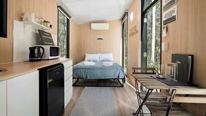 A compact hotel room with a bed, a small kitchenette, a dining table, and a large window providing a view of the outdoors.