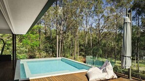 A swimming pool with a wooden deck, surrounded by trees.