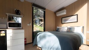 Une chambre avec un lit, un four à micro-ondes, un petit réfrigérateur et une fenêtre donnant sur un espace verdoyant.