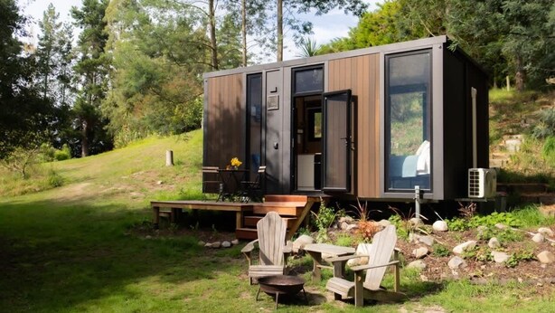 Une cabane moderne dotée d’une terrasse, de meubles d’extérieur et d’une grande fenêtre.