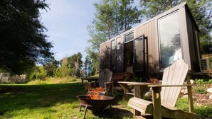 Une cabane moderne dotée d’une grande porte coulissante, d’un foyer extérieur et de coins salon aménagés à l’extérieur.