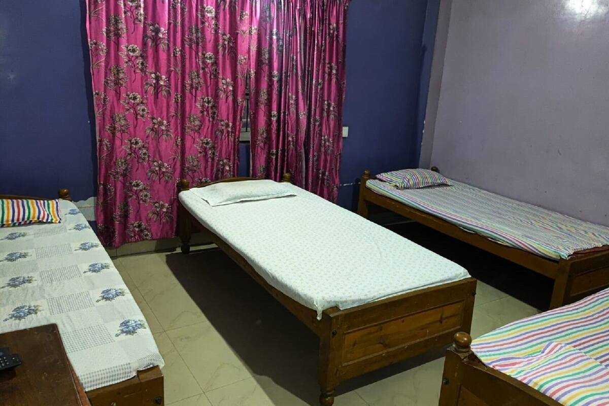 A room with two single beds, a wooden bed frame, a striped bedspread, and a floral curtain.