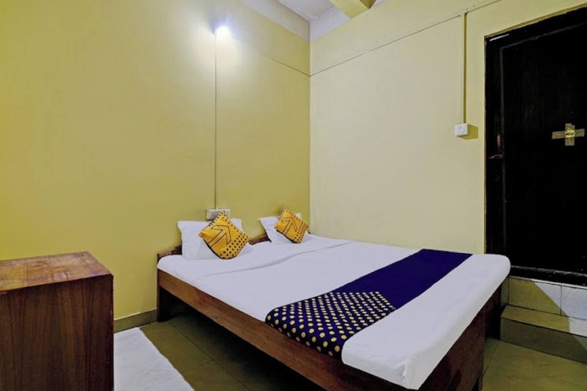 A single bed with white bedding and a blue accent, two pillows with yellow patterns, a wooden bedside table, and a black door.