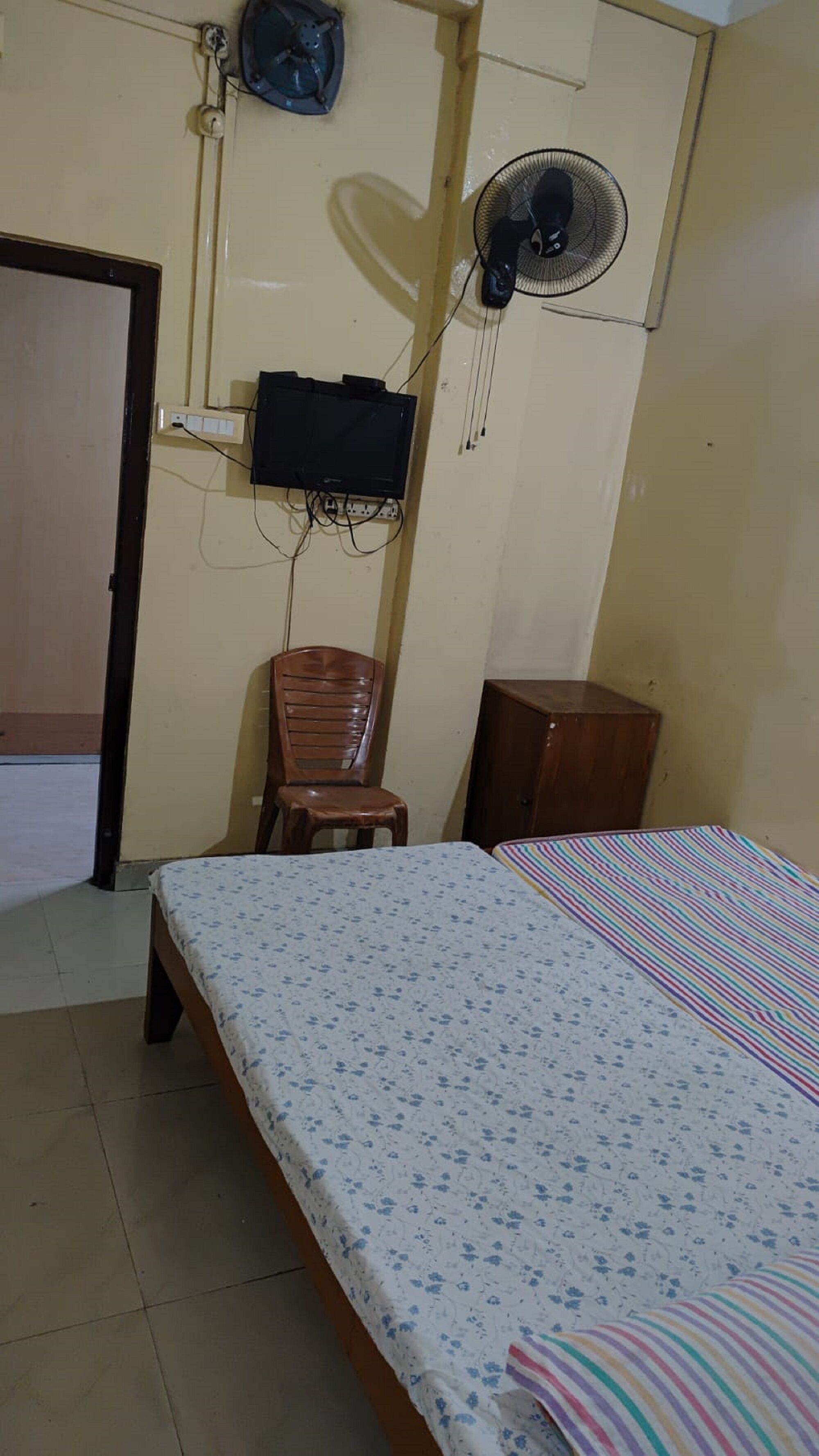 A bedroom with a bed, a chair, a TV, and a fan.