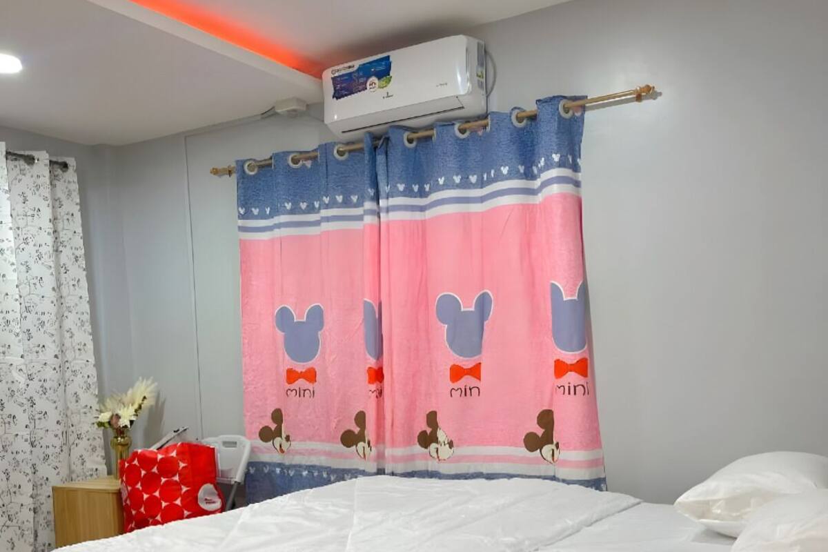Un dormitorio con cama, mesita de noche, un bolso rojo y aire acondicionado instalado en la pared.
