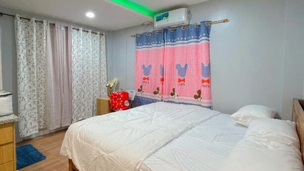 A bedroom with a bed, curtains, a dresser, and a blue rug. - DOS MARIAS TOURIST INN (Daanbantayan)