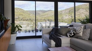 Un salon moderne doté d’une grande porte-fenêtre coulissante donnant sur un balcon. La pièce est aménagée avec un canapé beige agrémenté de plusieurs coussins, une table basse en bois et plusieurs plantes en pot.