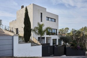 Une maison moderne à deux étages, dotée d’un toit plat, d’une grande fenêtre et d’un grand arbre à l’avant.